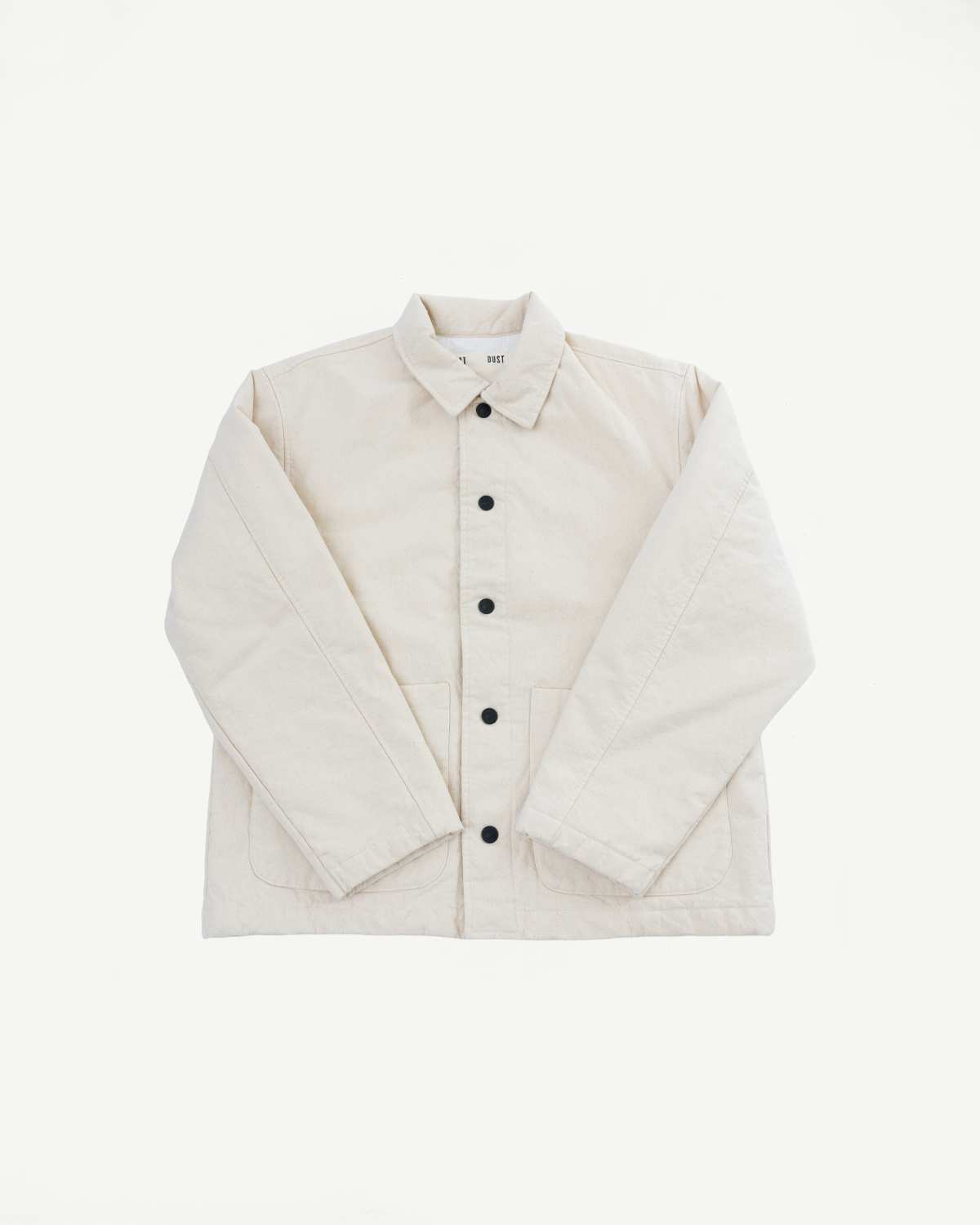Flat lay of ecru canvas jacket front, showing collar, black buttons, long sleeves, front pockets.