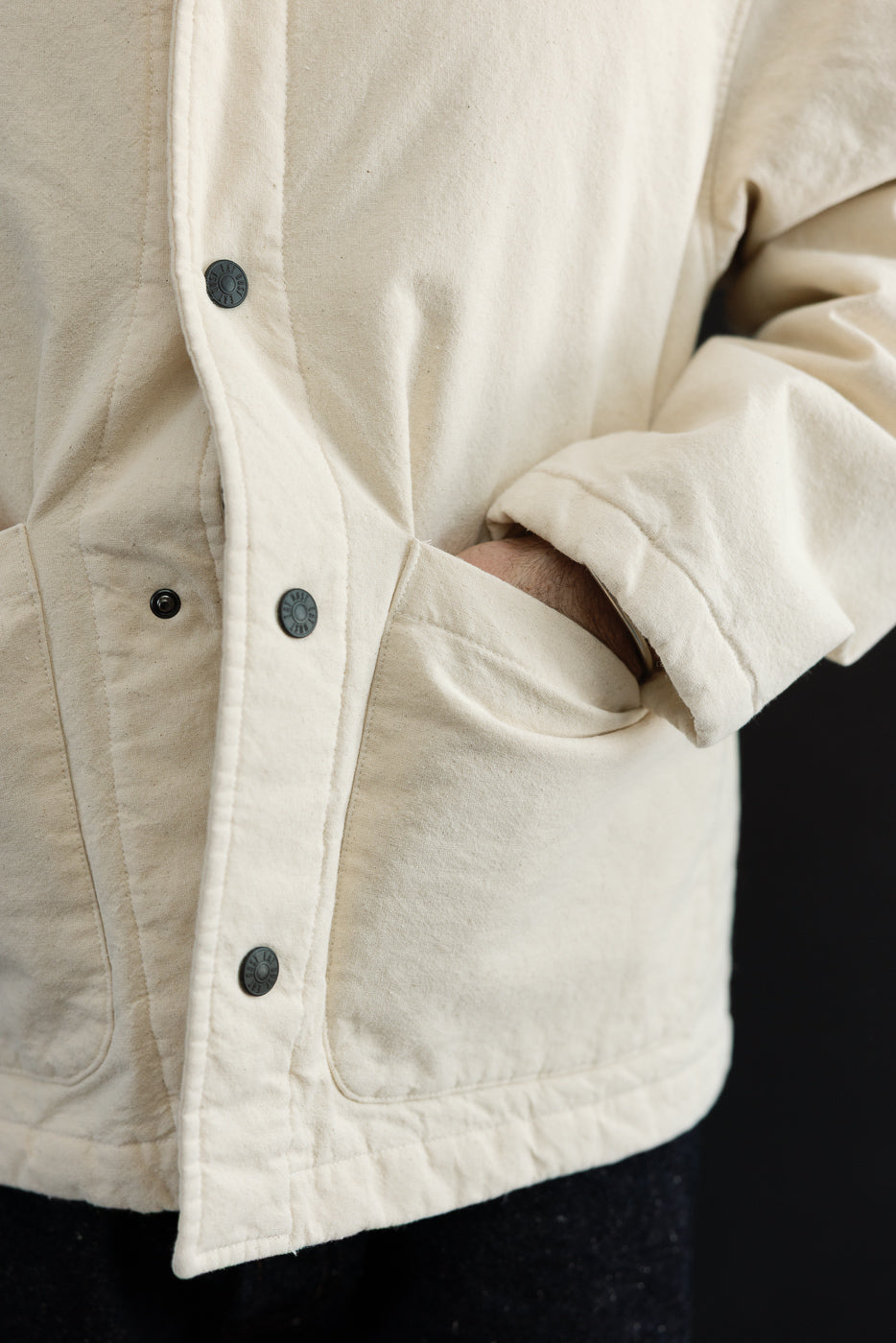 Close-up of front left side of ecru jacket on male model, showing snap buttons, pocket, and fabric texture, model is 5'9