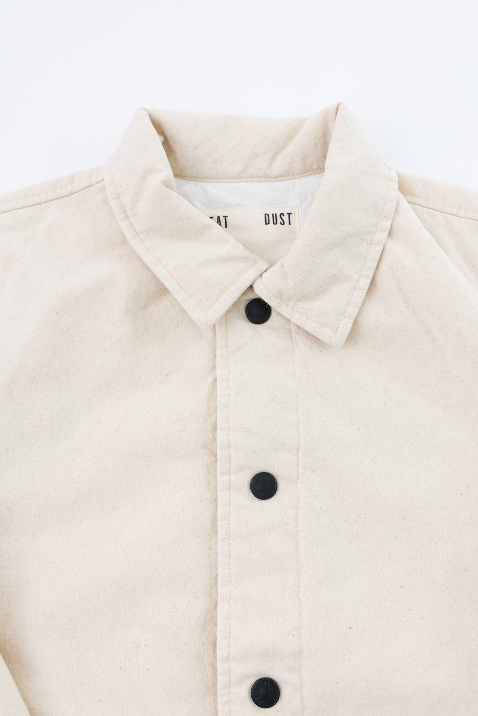 Close-up of front upper section of ecru jacket showing collar, buttons, and chest fabric texture