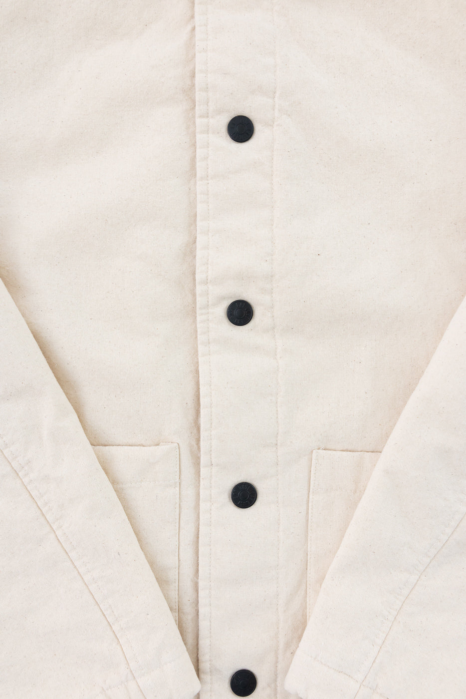 Close-up of front ecru jacket, showing black buttons, fabric texture, and front pockets.