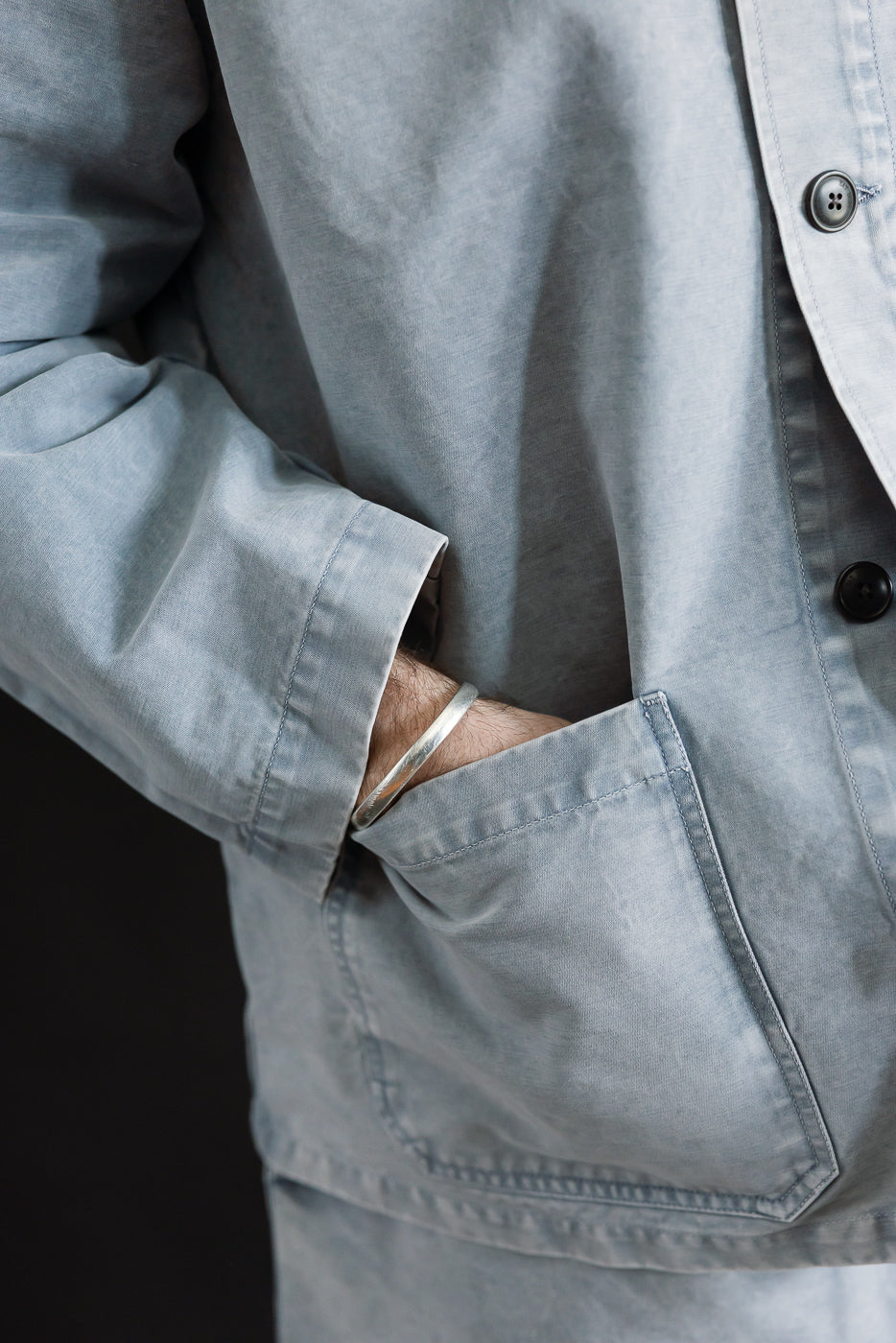 M-B-006 - Coach Jacket Nebraska Cotton - Coastal Blue: Close-up of a light gray-blue chore coat with patch pocket, silver cuff, and dark buttons, showcasing its worn, matte finish and relaxed fit.
