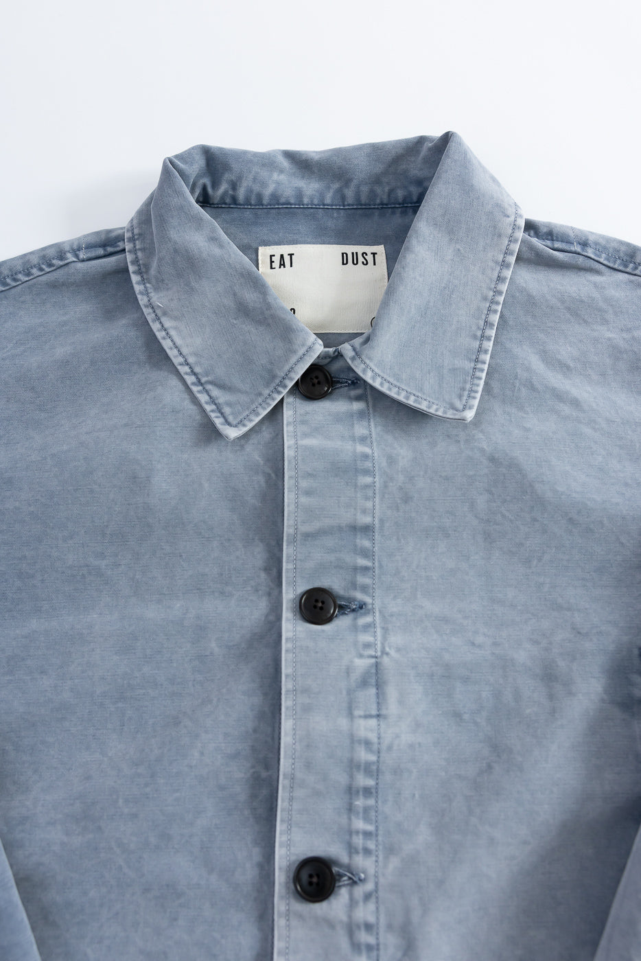 M-B-006 Coach Jacket Nebraska Cotton in Coastal Blue, featuring a light blue, button-up design with dark buttons, neat top-stitching, and an EAT DUST woven label inside the collar.