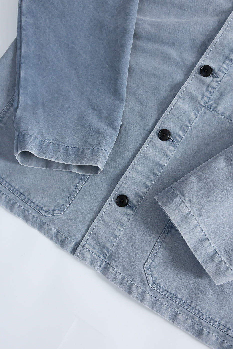 M-B-006 - Coach Jacket Nebraska Cotton - Coastal Blue: A light, washed-blue chore-style jacket with three dark buttons, two angled patch pockets, visible topstitching, and a relaxed fit. Made from 100% specialty Nebraska Cotton.