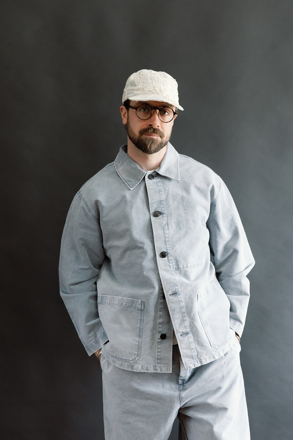 A bearded man models the M-B-006 - Coach Jacket Nebraska Cotton - Coastal Blue, showcasing its relaxed fit and chore-style design with hands in pockets and a confident, relaxed stance.