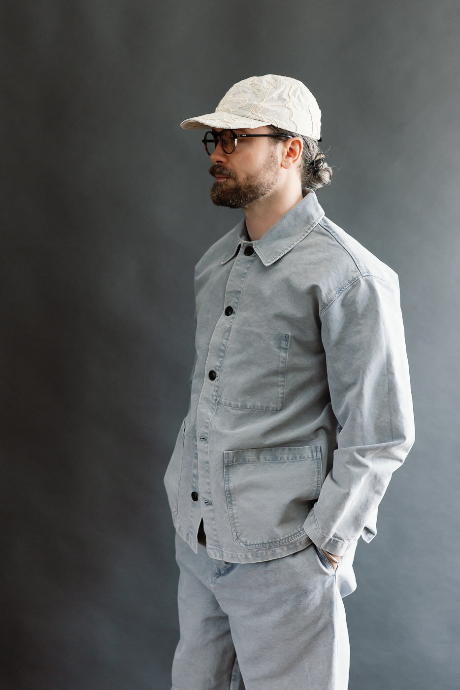 Man in profile wearing the M-B-006 Coach Jacket Nebraska Cotton - Coastal Blue, featuring a relaxed fit with large front pockets, styled with matching pants, embodying Dant's heritage-inspired workwear aesthetic.