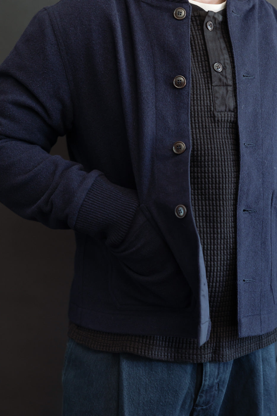 Close-up front view of a male model wearing a navy wool bomber jacket over a black waffle knit shirt.