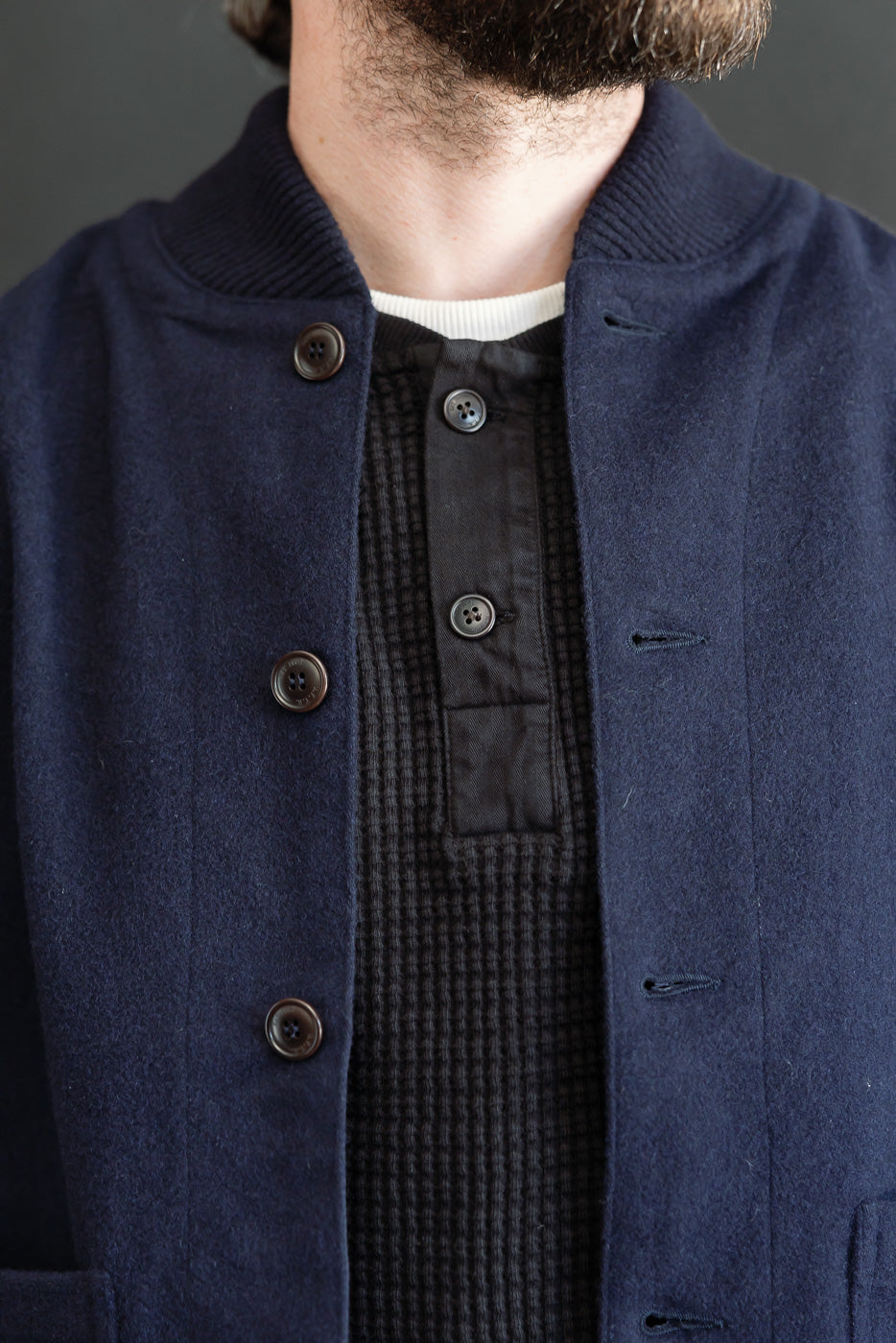 Close-up front view of a navy wool bomber jacket with dark brown buttons over a black waffle knit shirt.