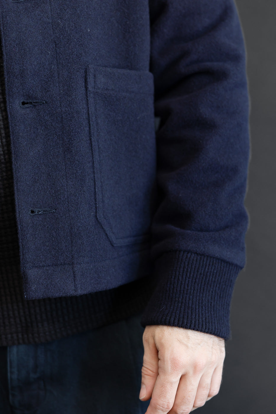 Close-up side view of a navy wool jacket showing the pocket, ribbed cuff, and fabric texture.