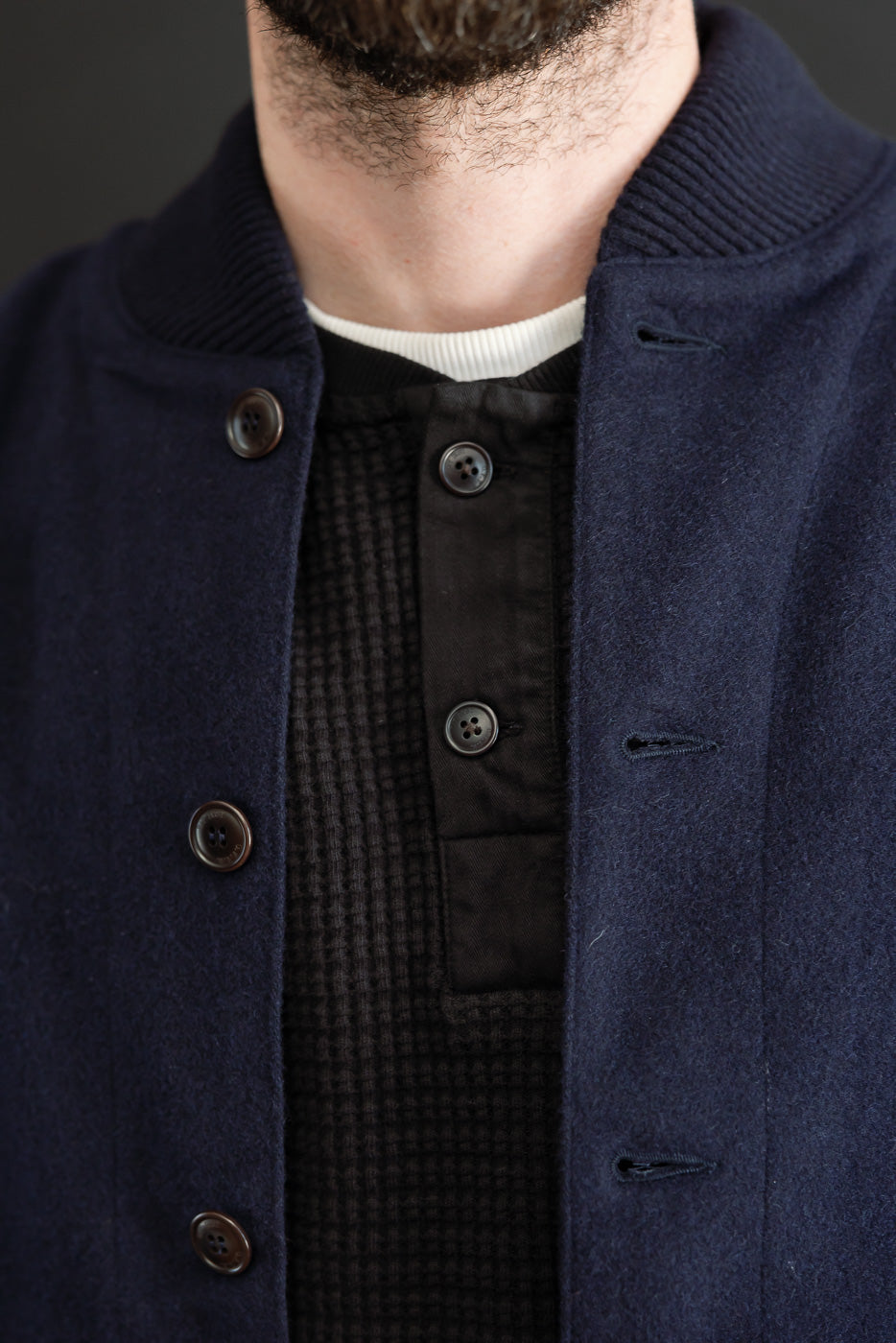 Close-up front view of a navy wool jacket showing button details and textured black henley.