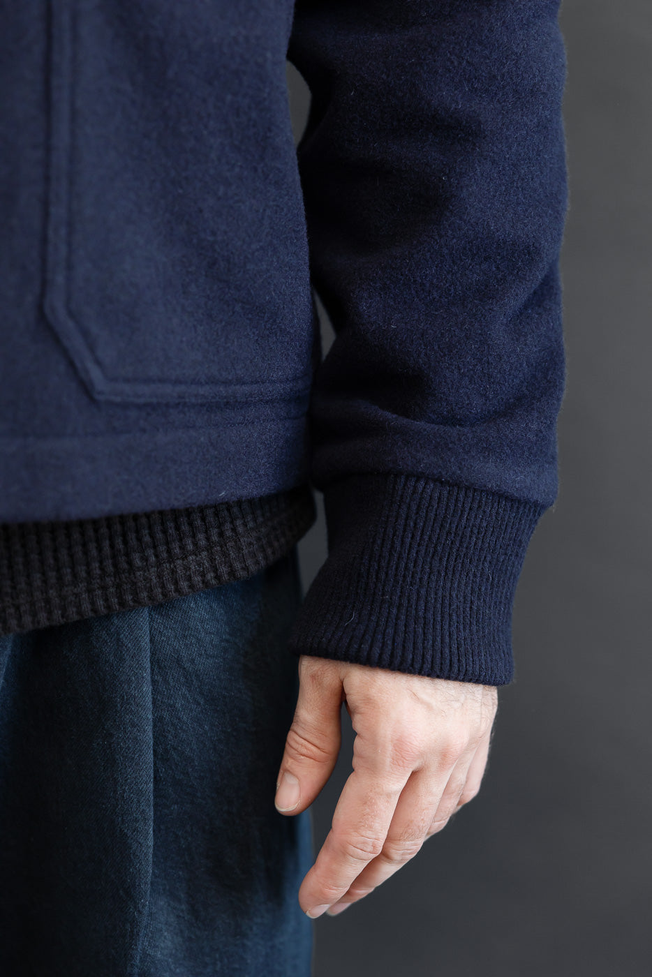 Close-up of the left sleeve and ribbed cuff of a navy blue wool jacket on a male model.