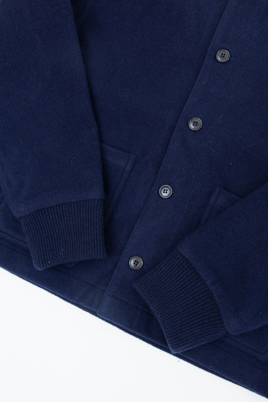 Close-up of the front of a navy blue cardigan showing buttons and ribbed sleeve cuffs.