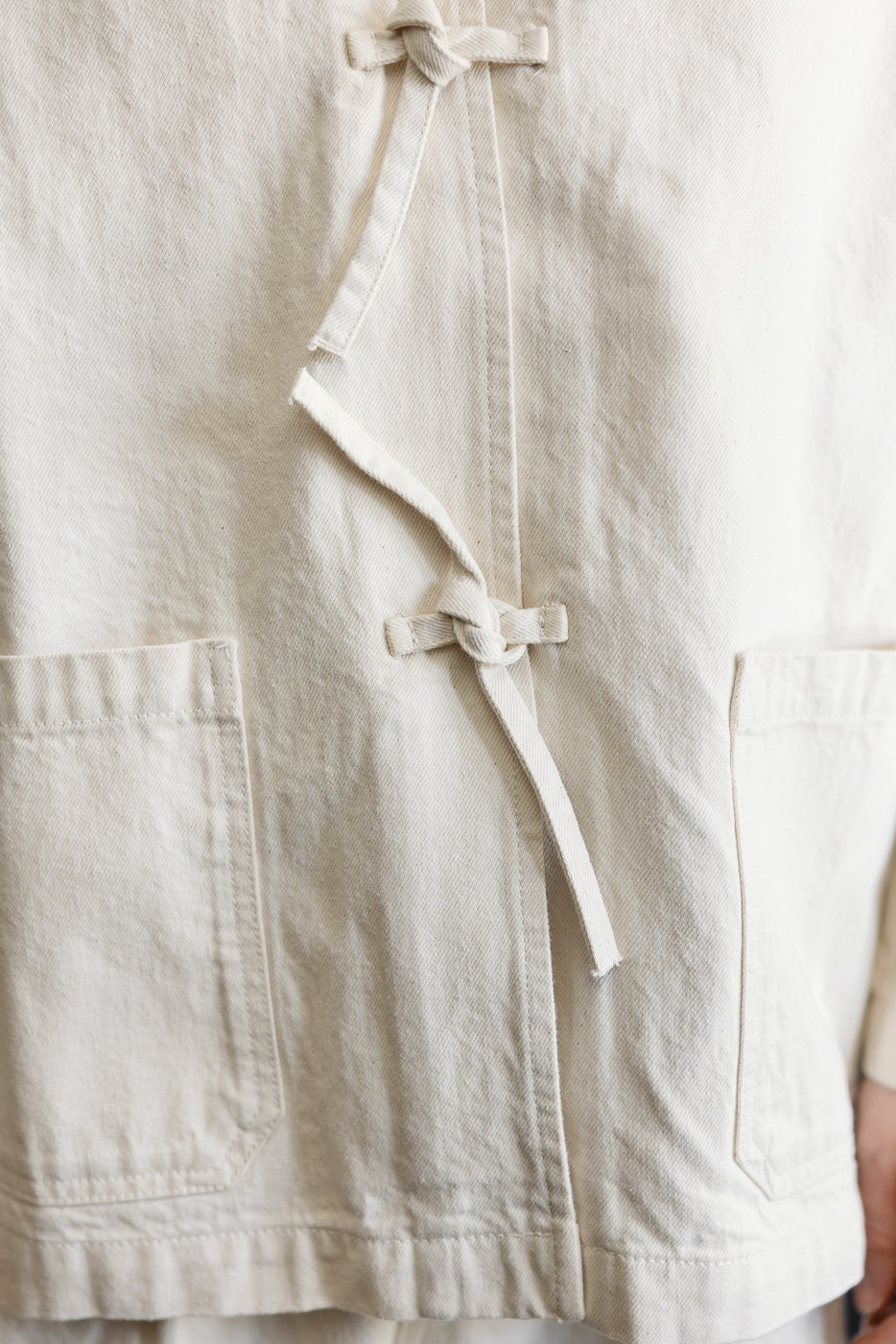 Close-up of ecru men's jacket front, showing tie closures, front pockets, and textured fabric