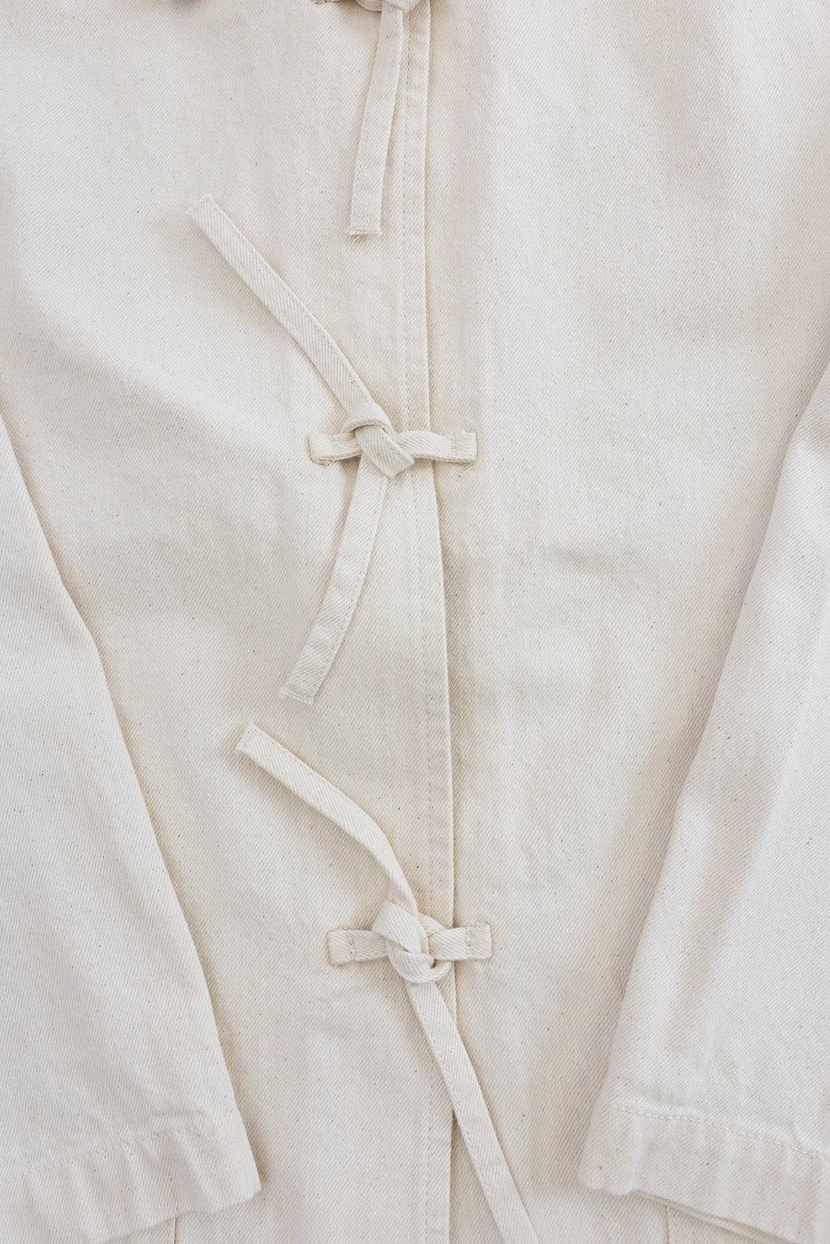 Close-up of front ecru jacket, showing fabric texture and knotted tie closures.