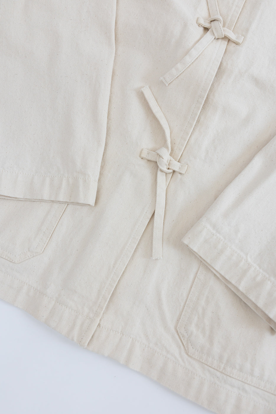 Close-up of ecru jacket front, showing fabric texture, tied front closures, and bottom pocket details.