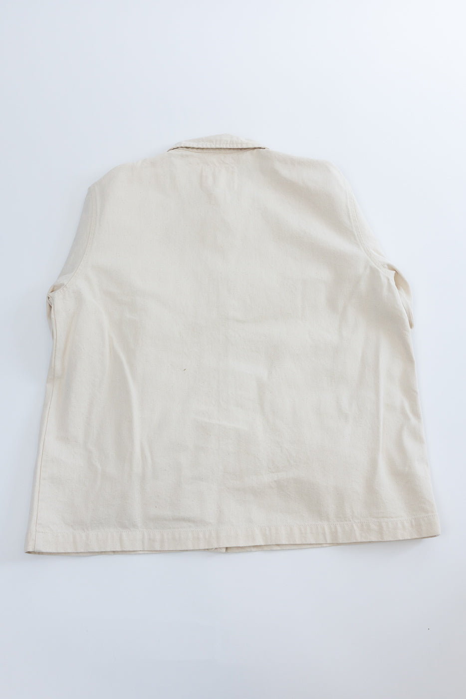 Flat lay of ecru canvas jacket, back view, showing straight hem and textured fabric.