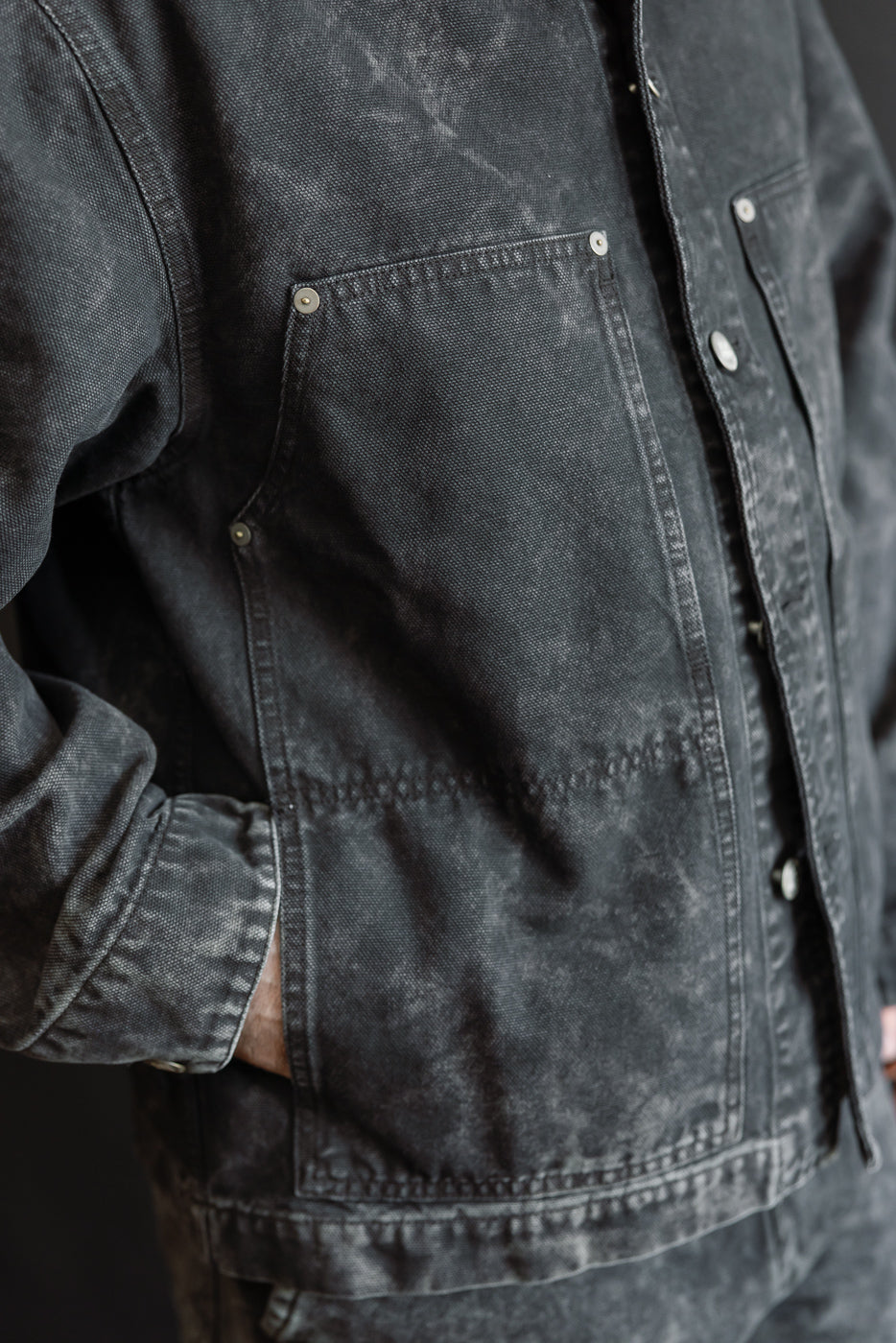 Close-up of front left side of men's canvas jacket, showing button details and pocket texture, worn by male model 5'9