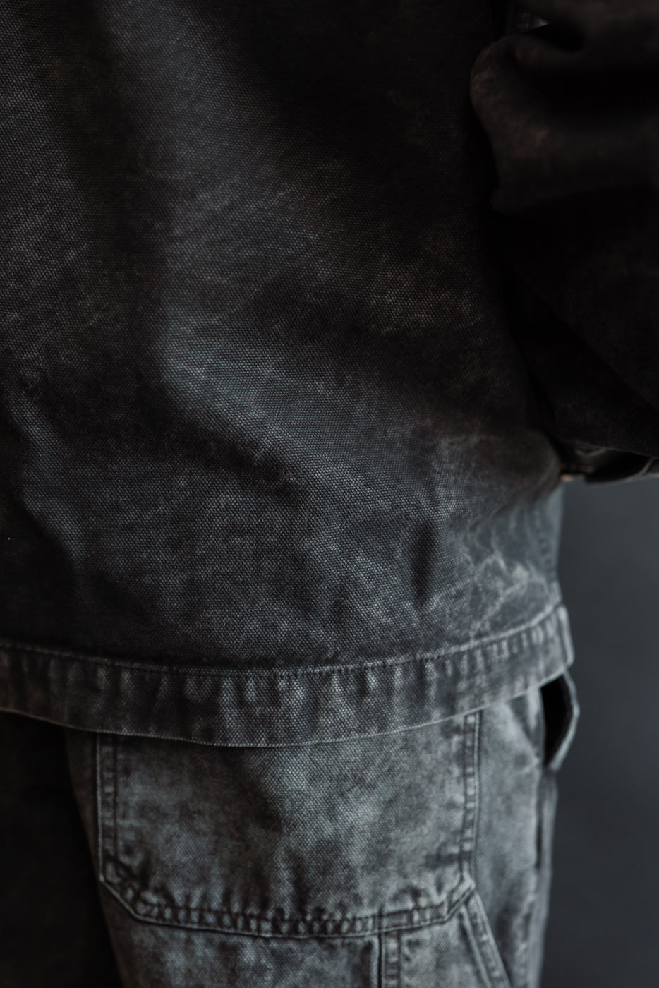 Close-up of canvas jacket hem and upper pant detail, showing fabric texture, left side.