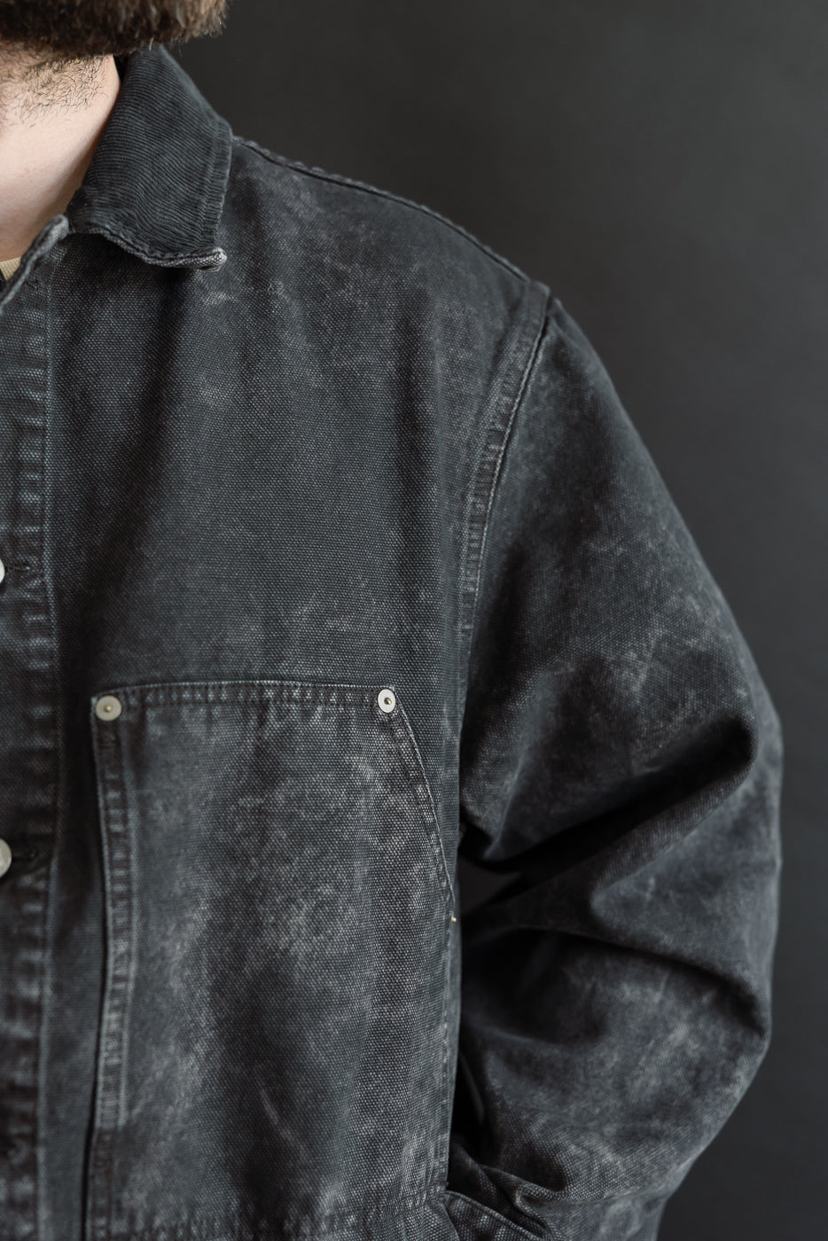 Close-up of front left chest and shoulder of men's canvas jacket, black wash, shown on male model 5'9
