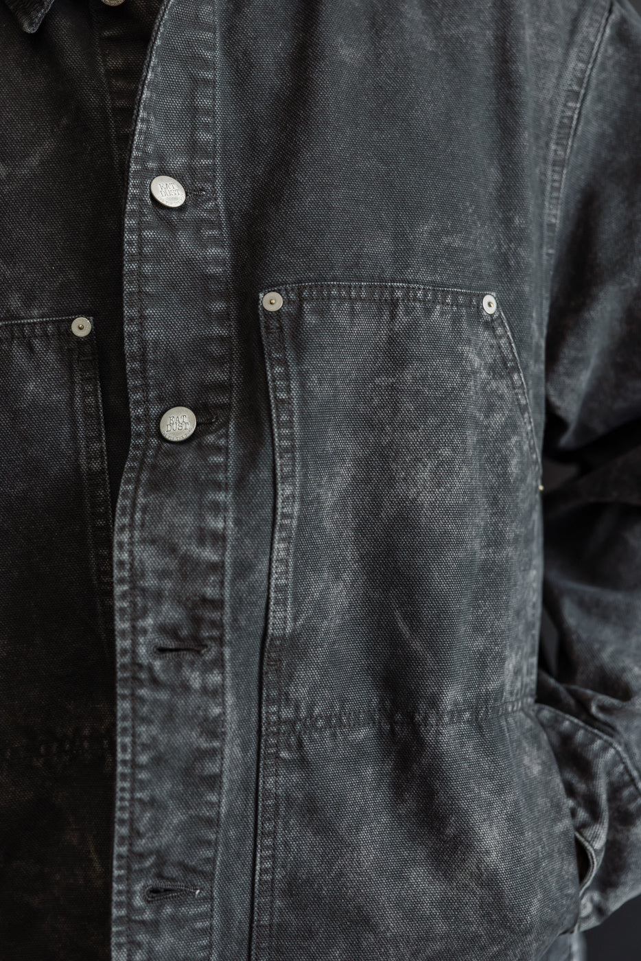 Close-up front view of men's Arizona canvas jacket in asphalt, showing chest pockets, metal buttons, and textured fabric. Male model, 5'9