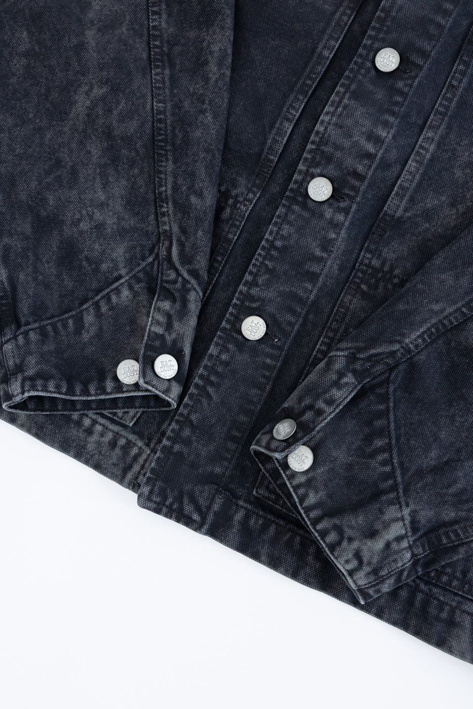 Close-up of men's black canvas jacket front hem and button details, flat lay view.