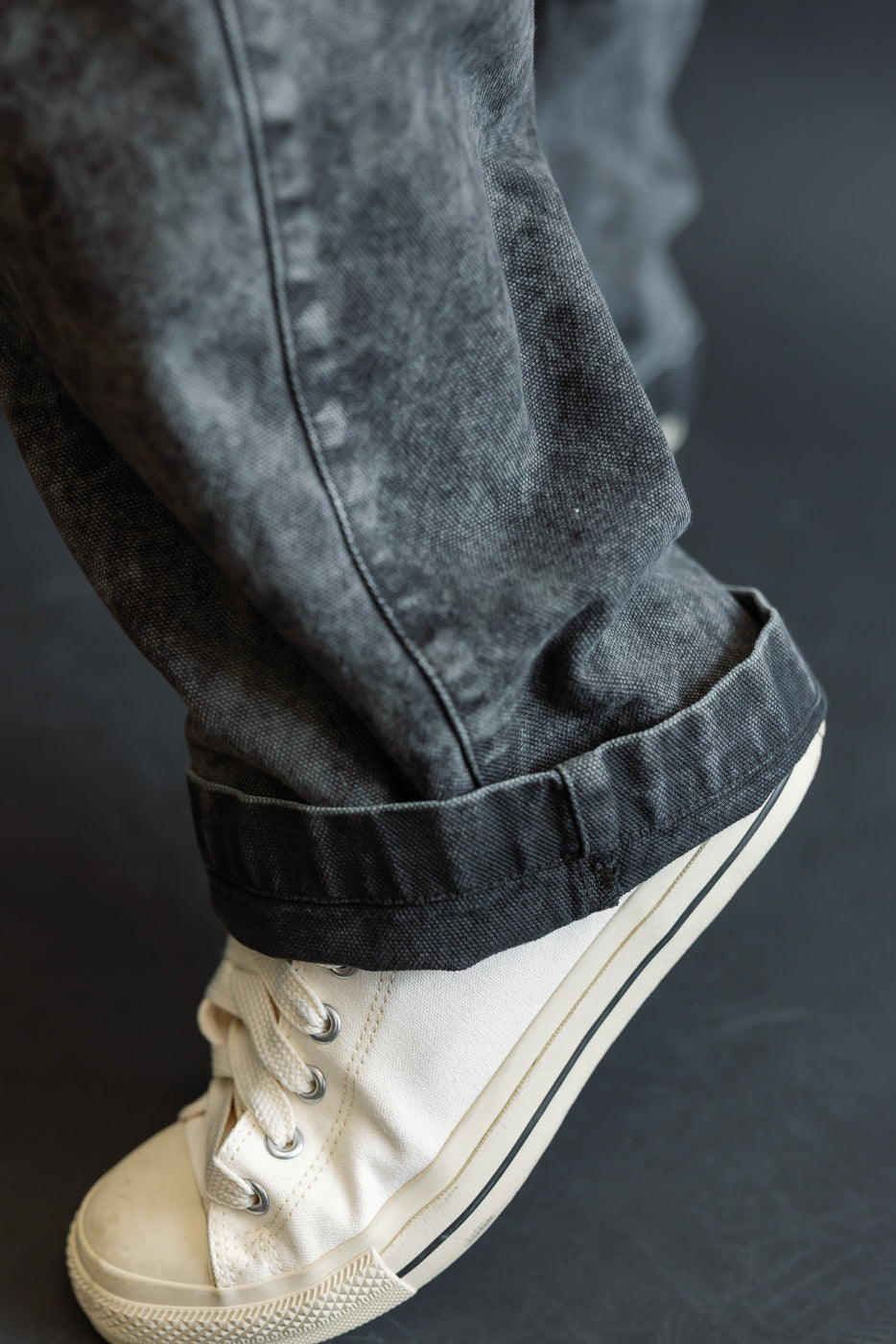 Close-up of male model's lower leg, showcasing cuffed hem and canvas texture of asphalt chino pants, side view, 5'9