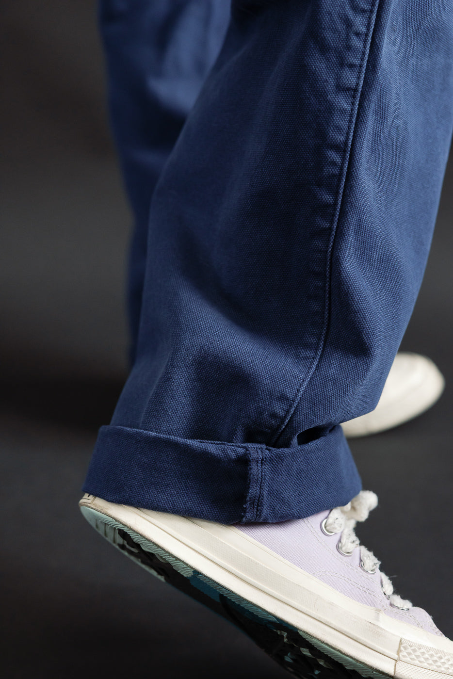 Close-up of male model's cuffed canvas indigo blue chino pant leg, left side, with sneaker; 5'9