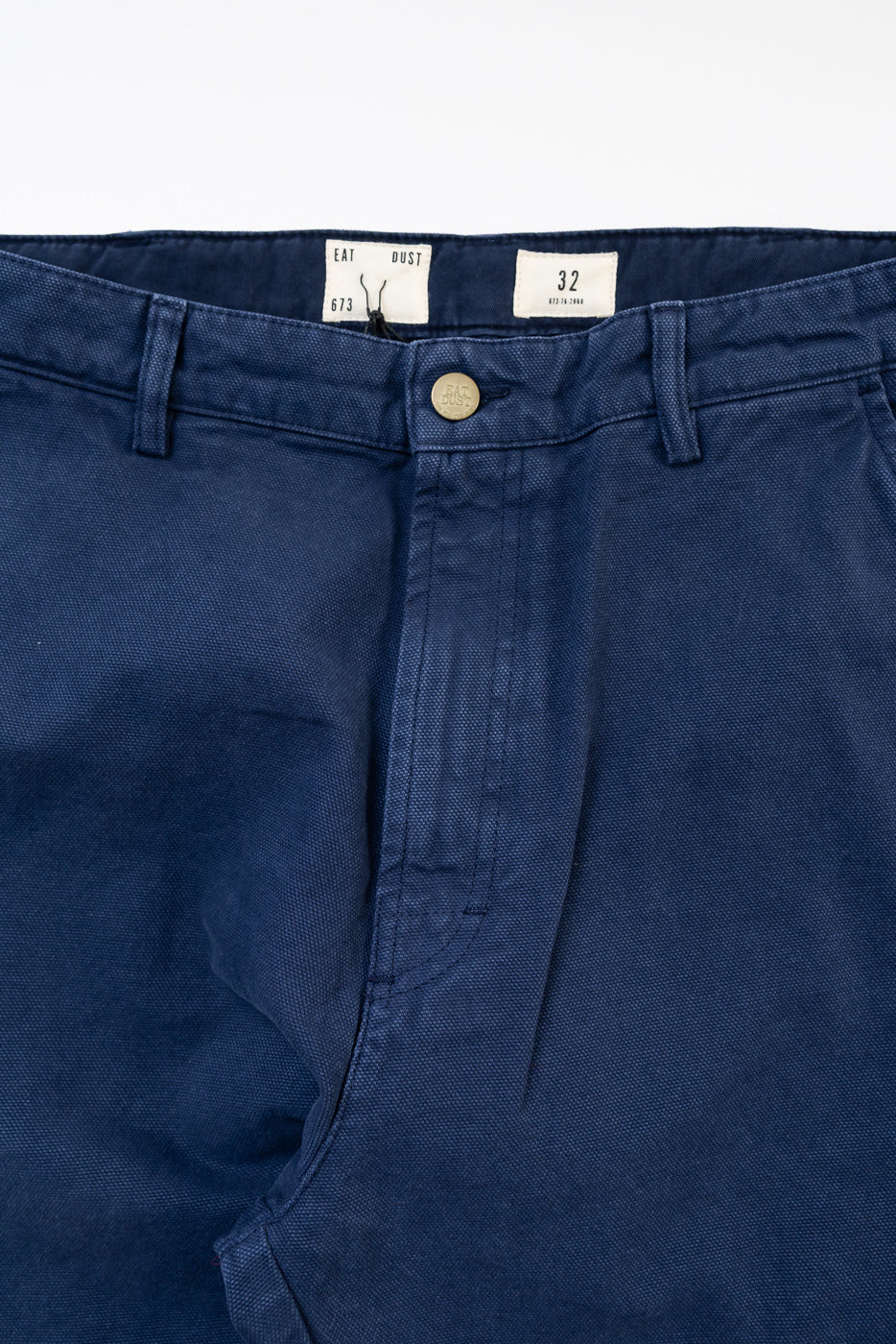 Close-up front view of indigo blue canvas Oakland chino pants, button and waistband detail.