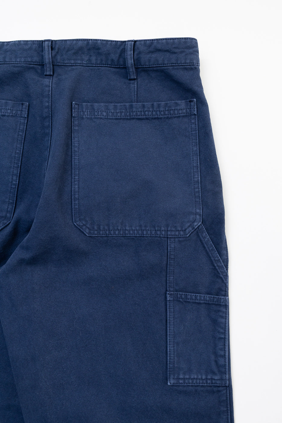 Close-up of back right side of indigo blue canvas chino, showing rear and side pockets
