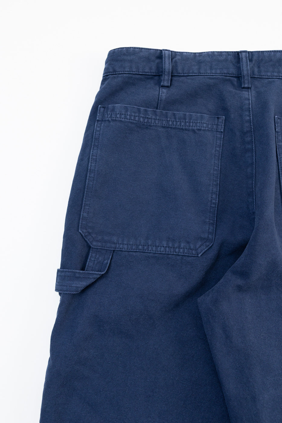 Close-up of back side of indigo blue canvas chino showing back pocket and belt loop detail