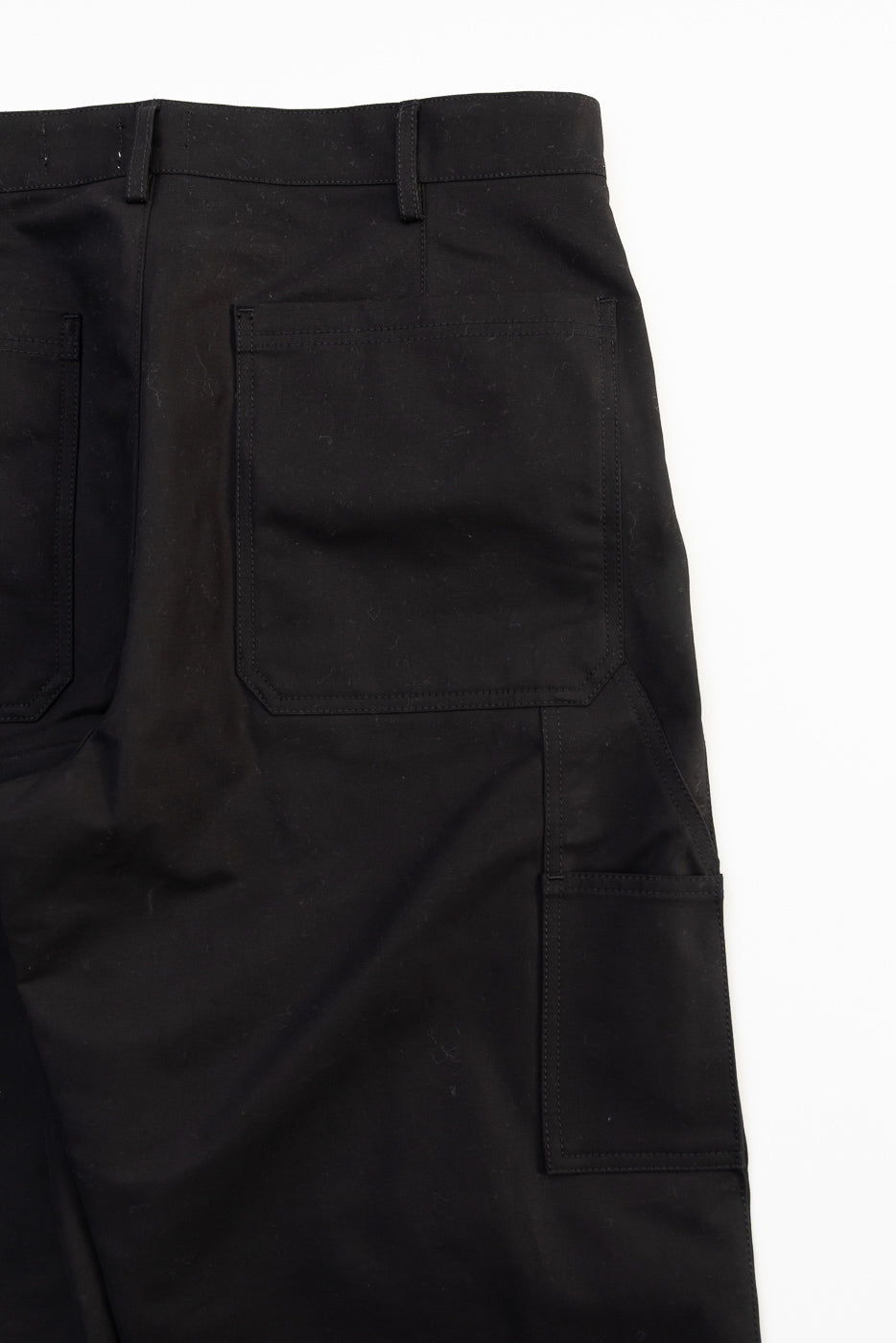 Close-up flat lay of black cotton Oakland Chino pants, front left side, showing front pocket detail.