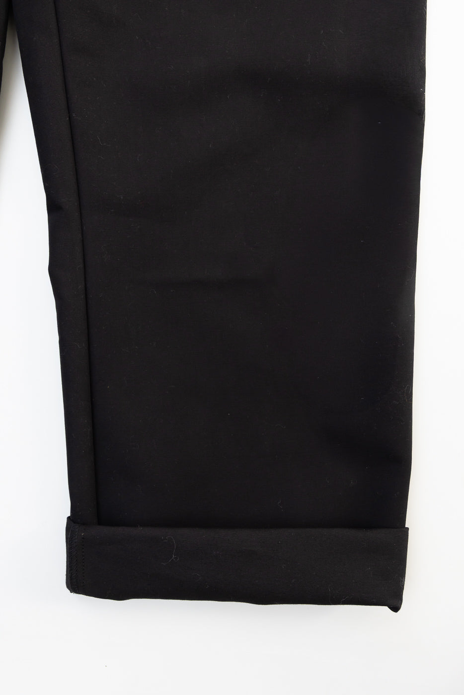 Close-up of front left leg cuff on black cotton chino pants, showing fabric texture and hem.