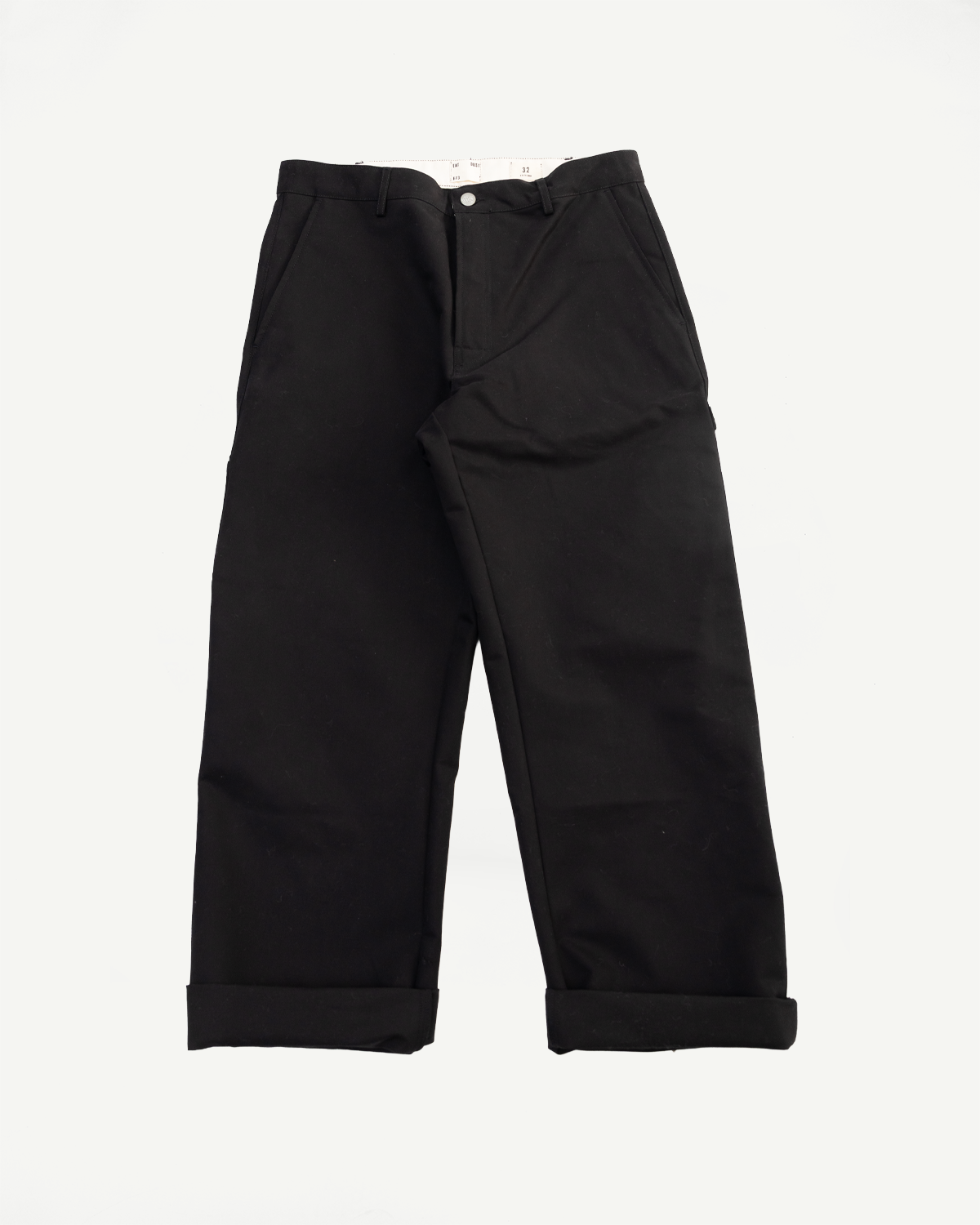 Flat lay front view of black cotton chinos with cuffed hem, belt loops, and button closure.