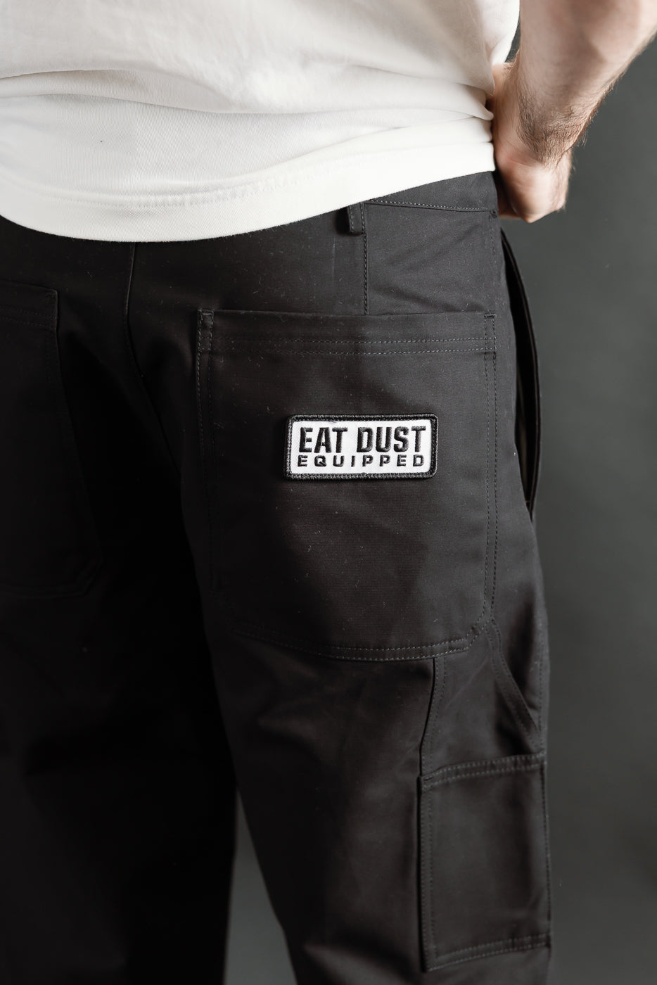 Close-up of back side of black Oakland chino pants with Eat Dust patch, on 5'9 male model