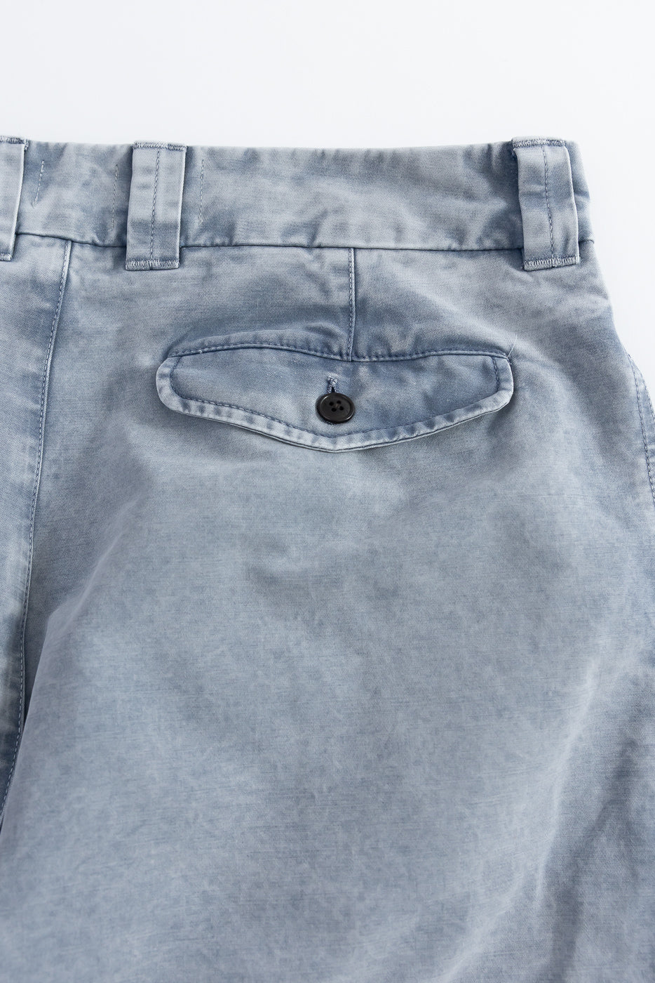 Close-up of back side of blue cotton chino pants showing buttoned pocket and belt loops.