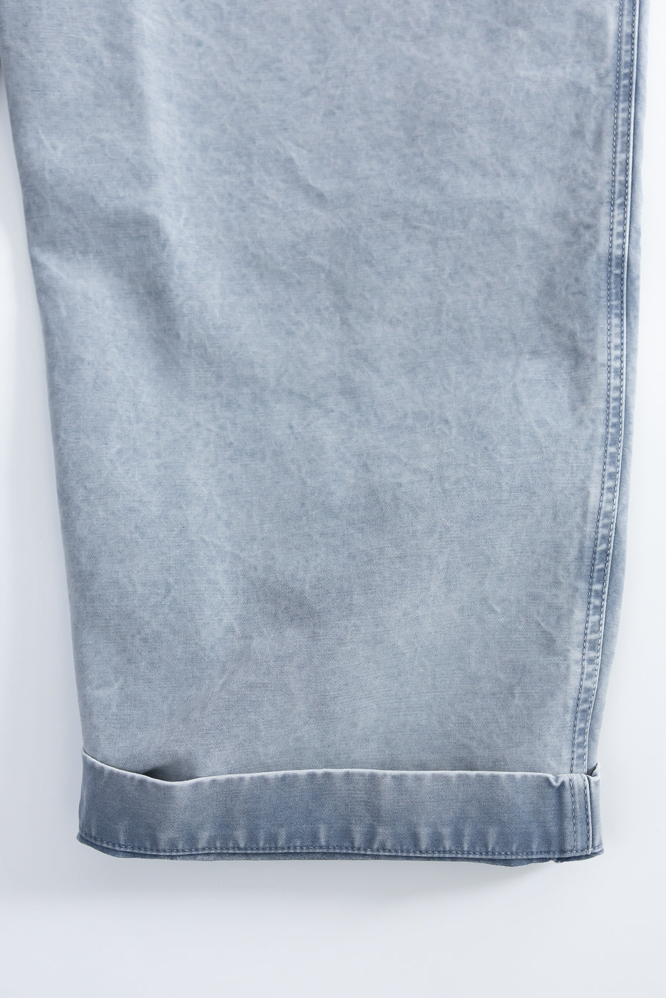 Close-up of the front lower leg and cuff of coastal blue cotton chino pants, showing fabric texture and stitching details.
