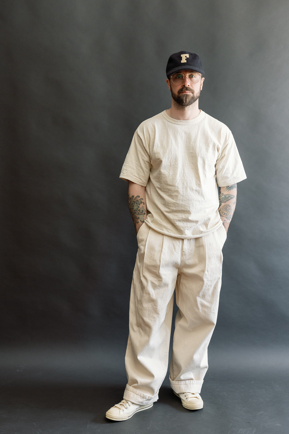 Full body front view of male model, 5'9, 165lbs, athletic build, wearing ecru canvas t-shirt and pleated pants.