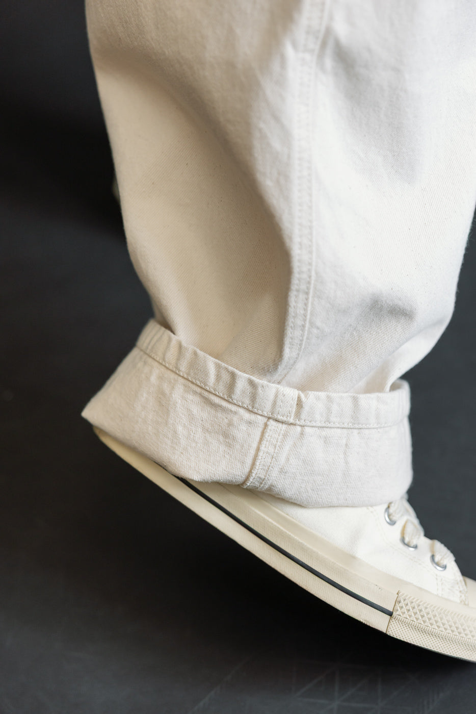 Close-up of men's ecru canvas pants cuff and sneaker, side view, fabric texture visible. Model is male, 5'9