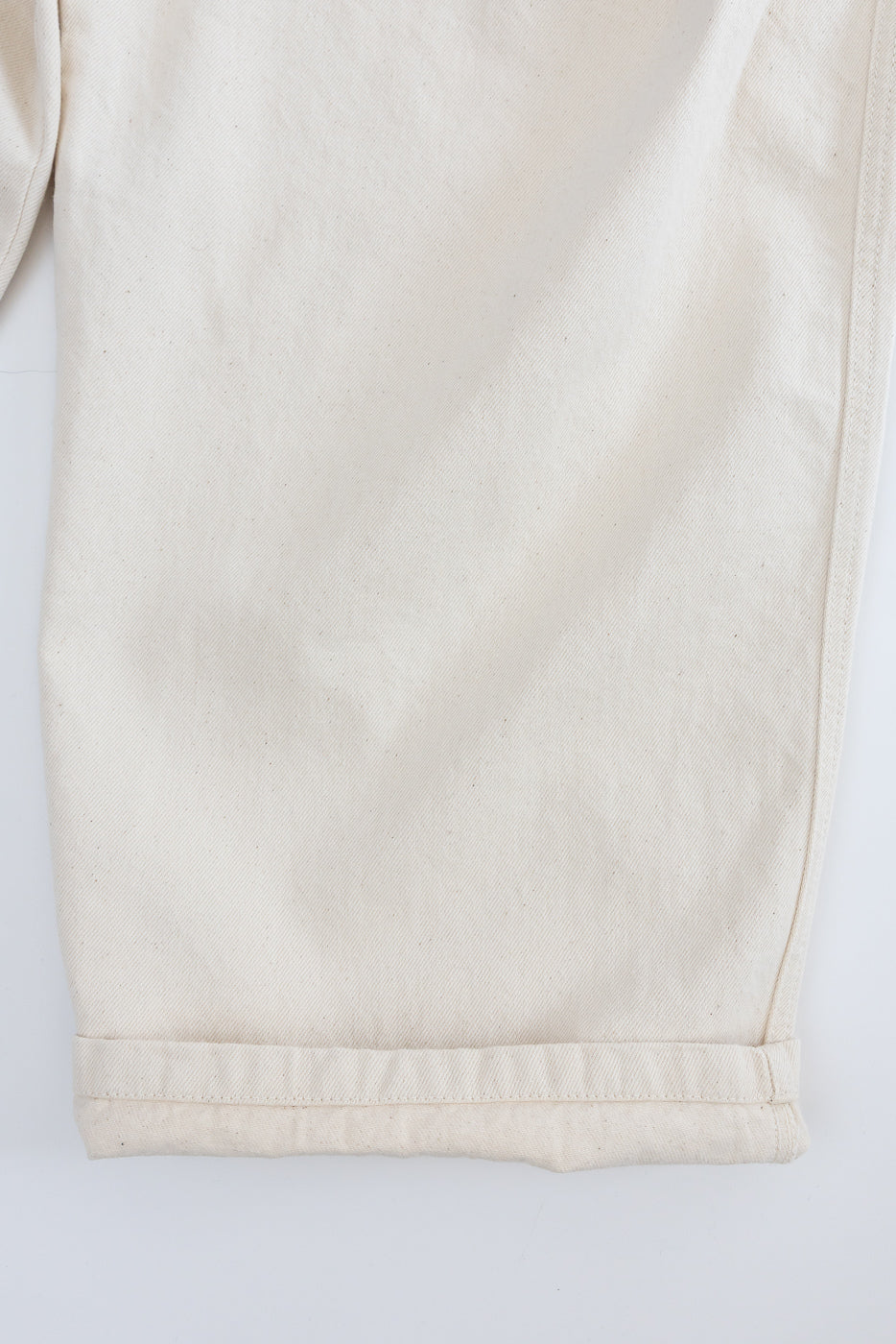 Close-up of front pant leg hem in ecru canvas, showing fabric texture and stitching details.