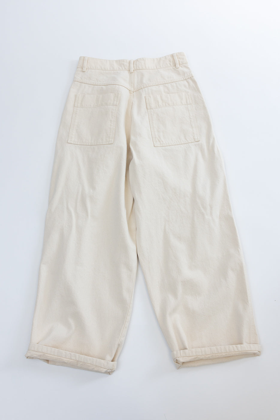 Flat lay of ecru canvas pants, back view, showing rear patch pockets and cuffed hems.