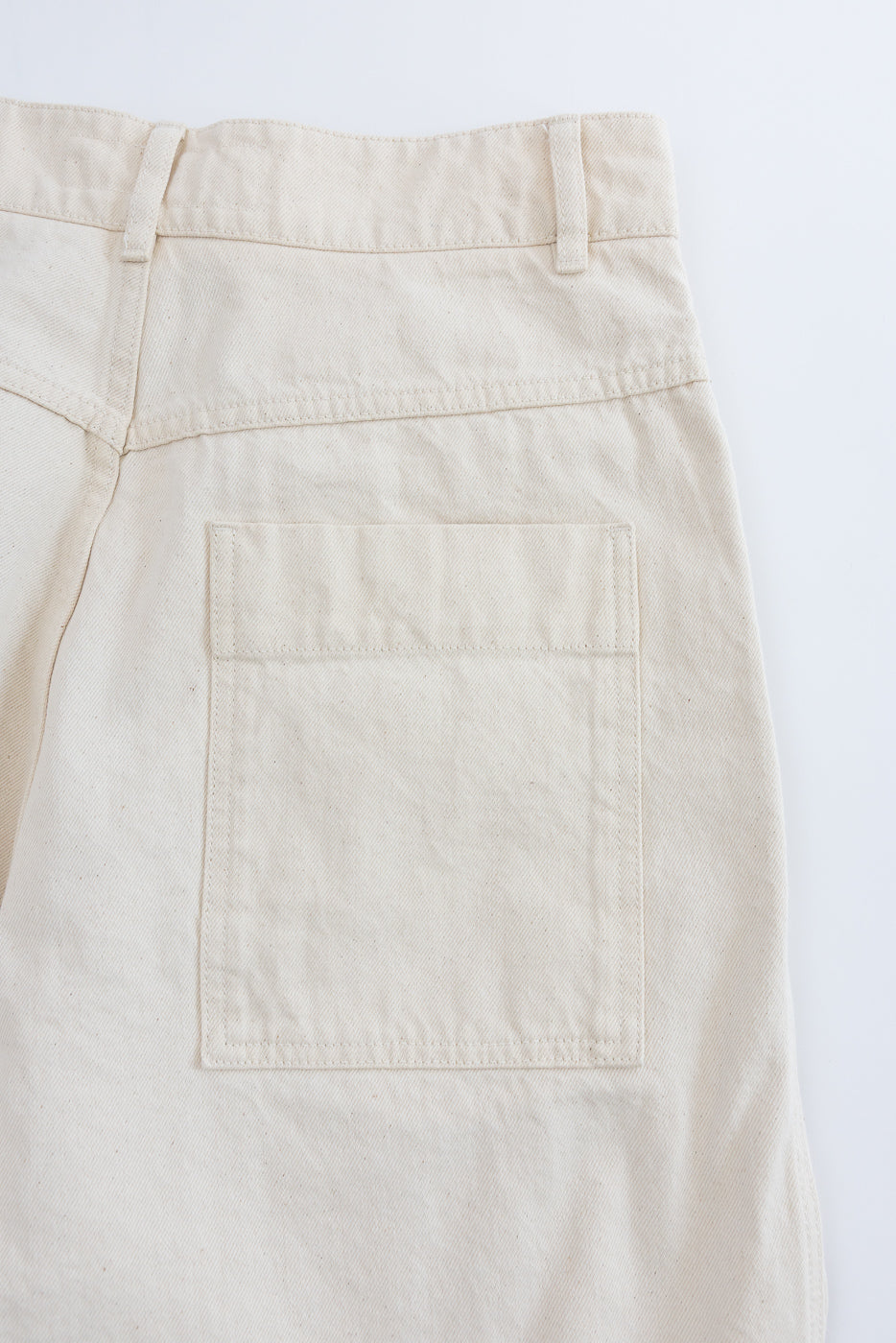 Close-up of ecru canvas pants, flat lay showing back side and single rear pocket detail.