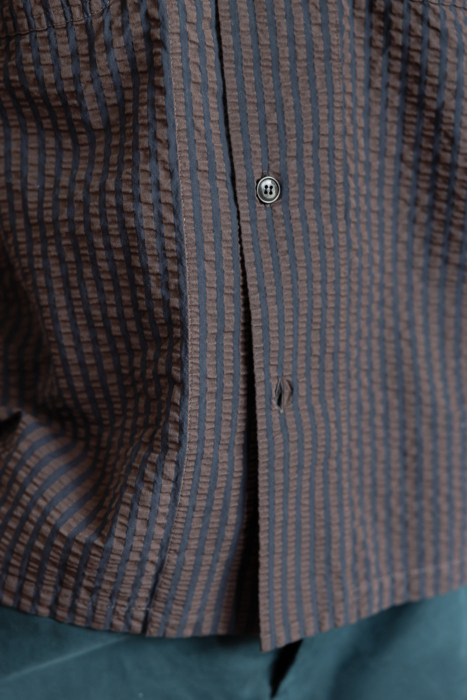 Close-up of front midsection of men's seersucker denim shirt, coffee and navy stripes, button detail