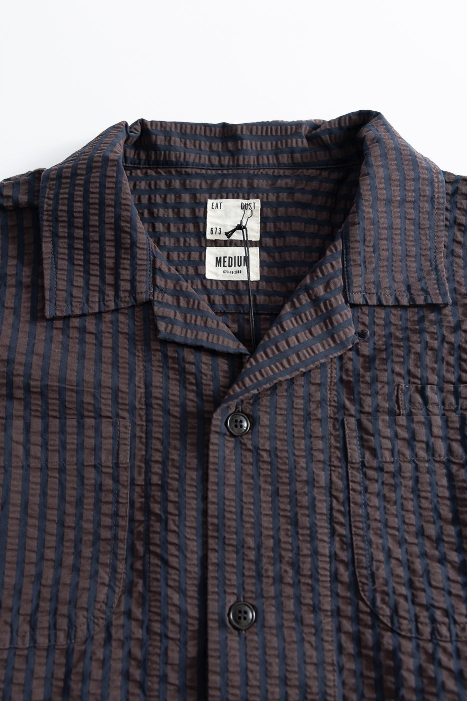 Close-up front view of men's coffee navy seersucker Aloha shirt, showing fabric texture, buttons, collar, chest pocket, and inner tag details.