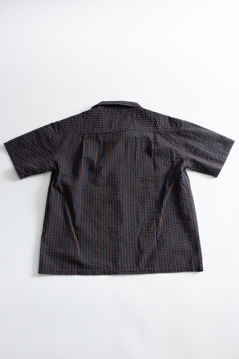 Flat lay of the back of a short sleeve seersucker denim aloha shirt in coffee and navy.