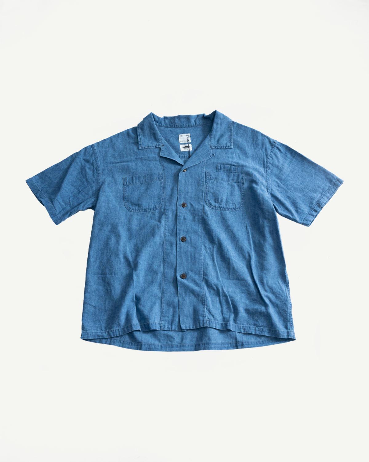 Flat lay front view of blue linen-cotton aloha shirt with short sleeves, open collar, chest pockets, and button details.