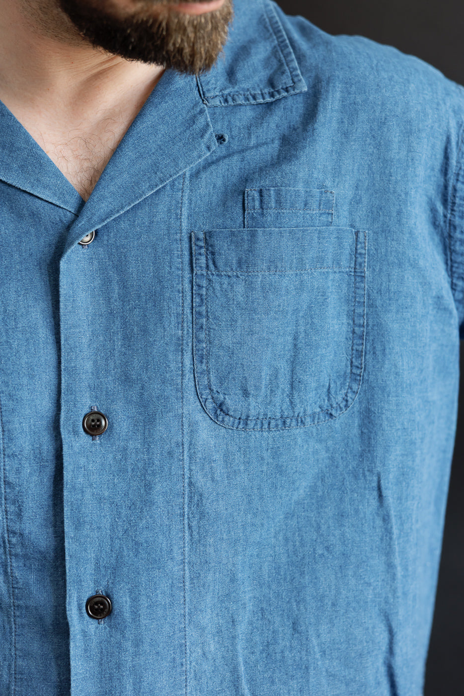 Close-up of front chest pocket and buttons on men's blue linen-cotton Aloha shirt, male model, athletic build.
