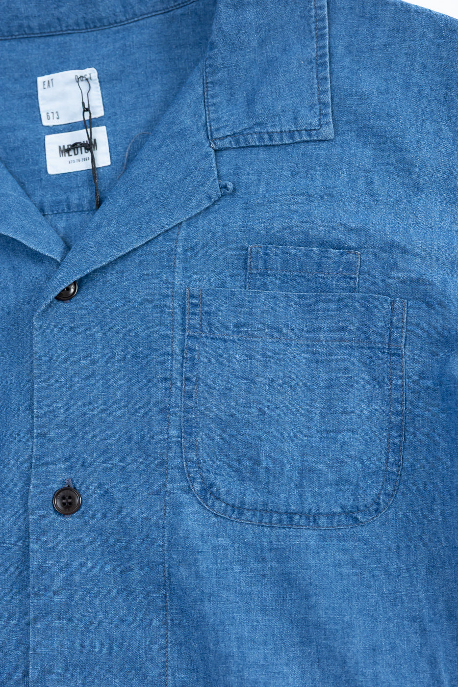 Close-up of front chest pocket, collar, and buttons on blue linen cotton denim Aloha shirt.