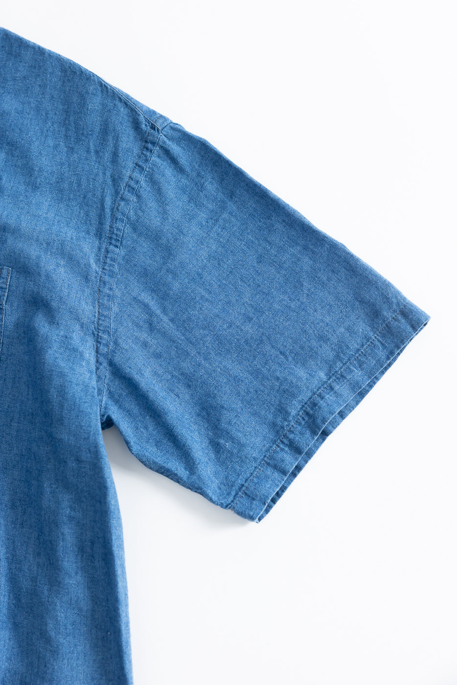 Close-up of right sleeve and shoulder seam of blue linen cotton denim aloha shirt, front view.