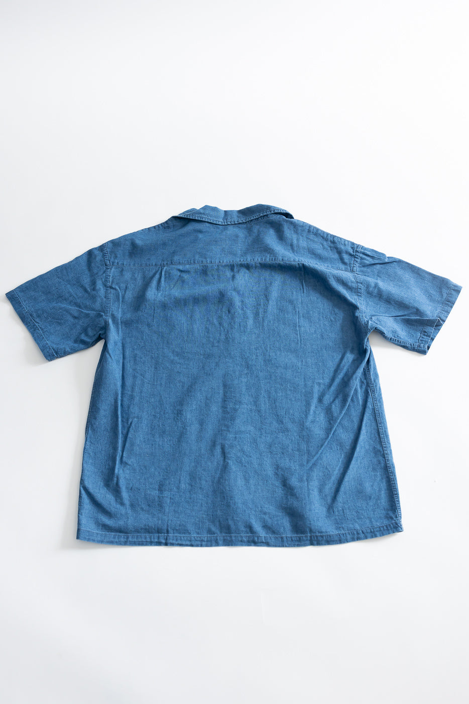 Flat lay of blue linen cotton denim aloha shirt, back view, showing short sleeves and collar.