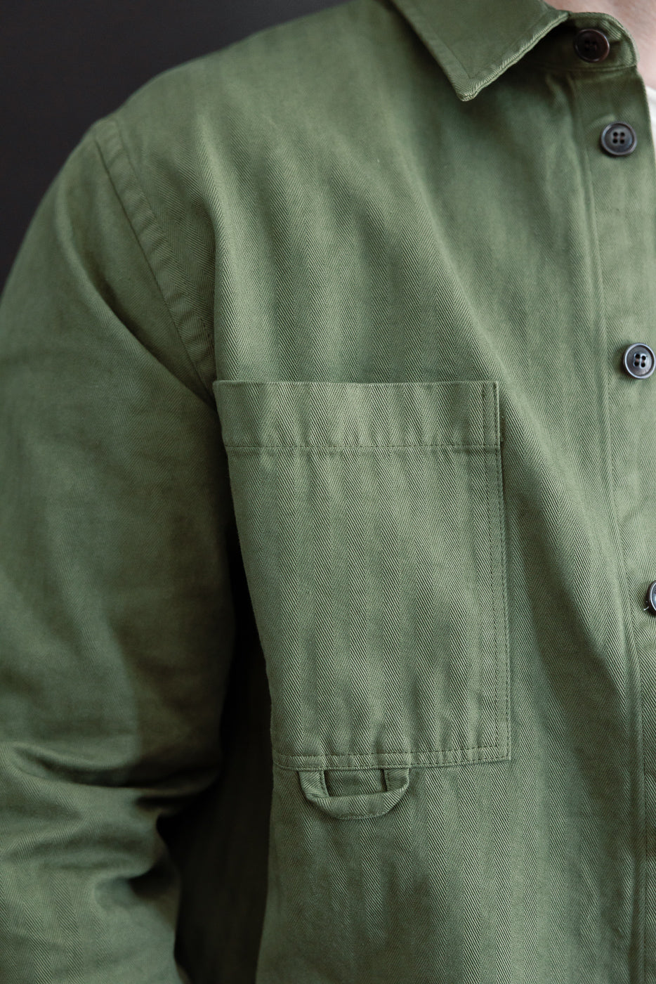 Close-up of the front right chest pocket and button placket of an olive green shirt.