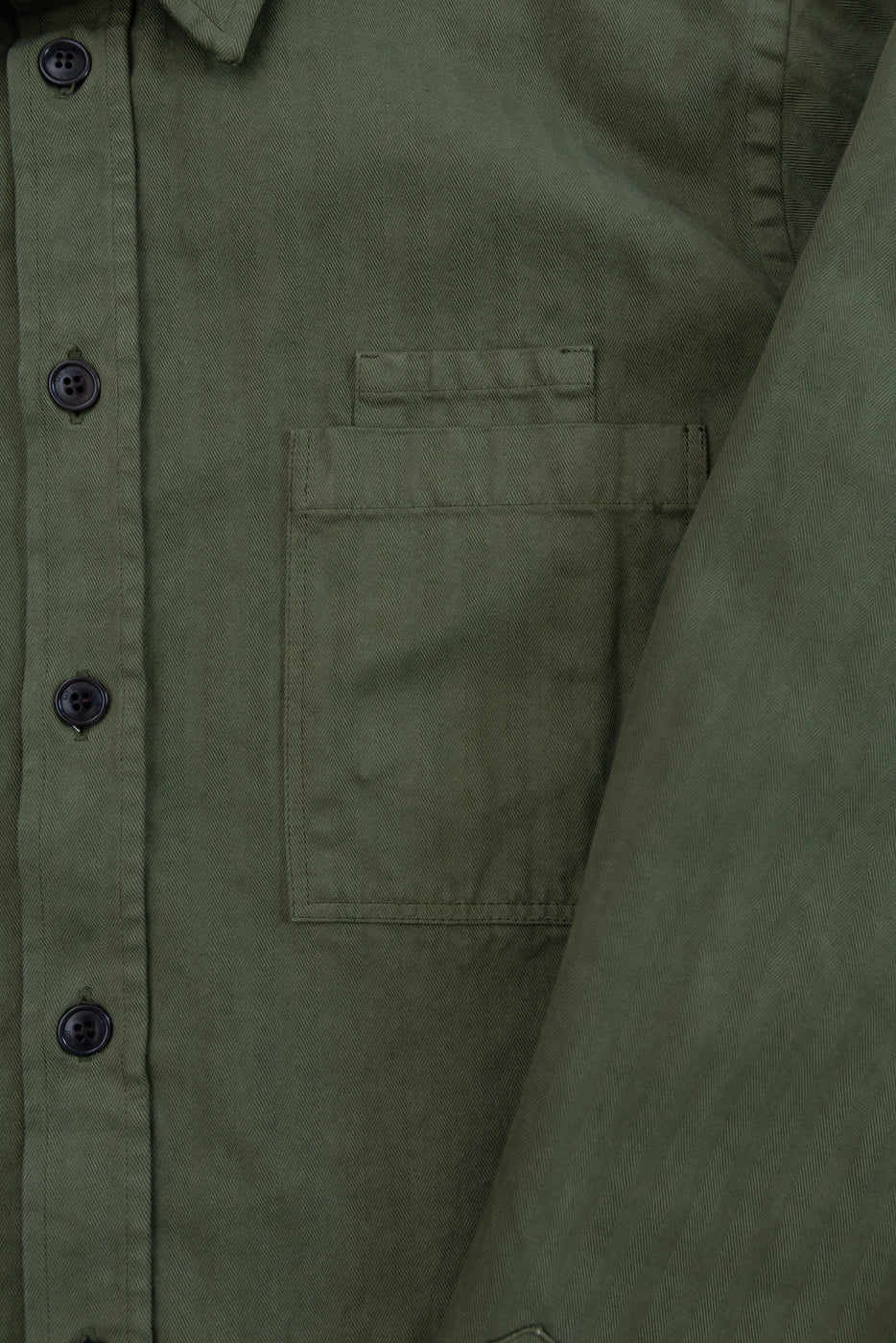 Close-up of the front of an olive green shirt showing buttons and chest pocket texture.